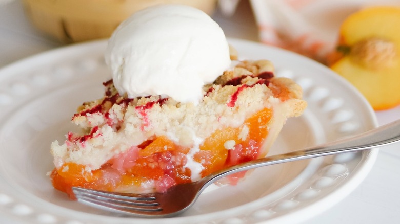 Slice of fruit pie on plate with fork and cream