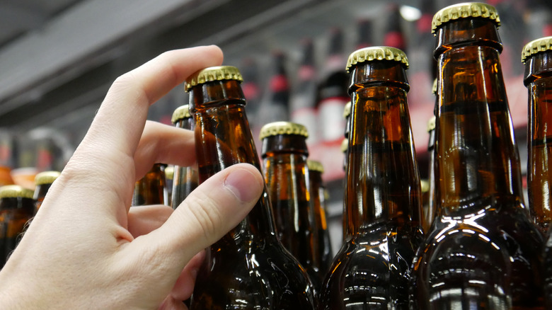 A close-up of a hand pulling a brown beer bottle from a shelf.