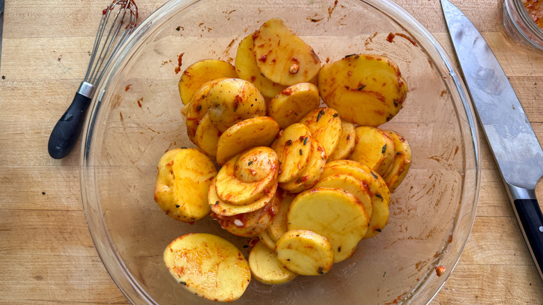 Sliced potatoes in bowl coated with sauce