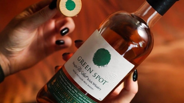 A person holding a bottle of Green Spot Single Pot Still up to the camera, with the green spot on top of the cork lid shown