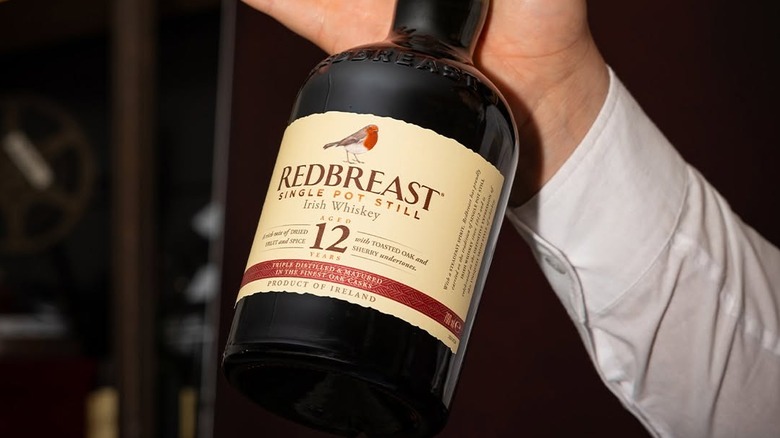 A bottle of Redbreast 12-year held up to the camera by someone in a dress shirt