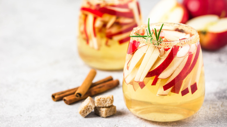 A sugar-rimmed glass with a golden apple cocktail and thin slices of apple garnish