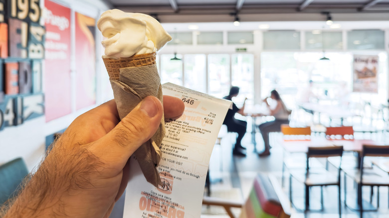 A hand holds an ice cream cone and a receipt from Burger King.