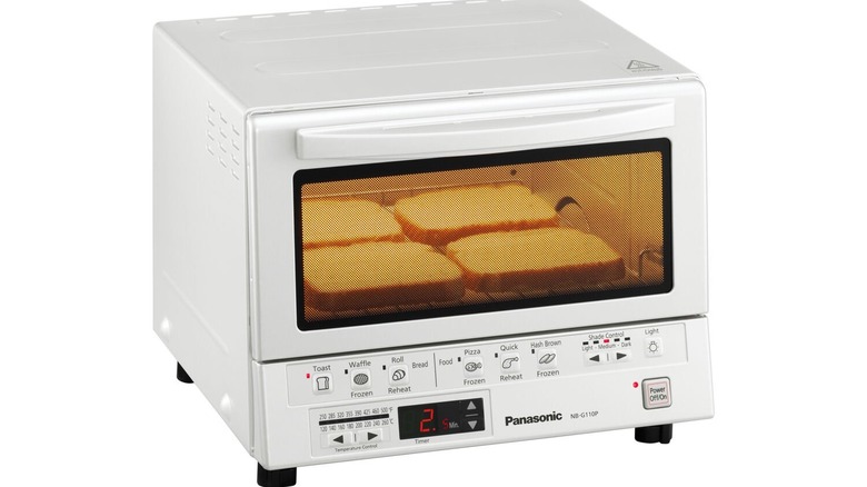 A minimalist white toaster oven with four slices of bread inside on a white background