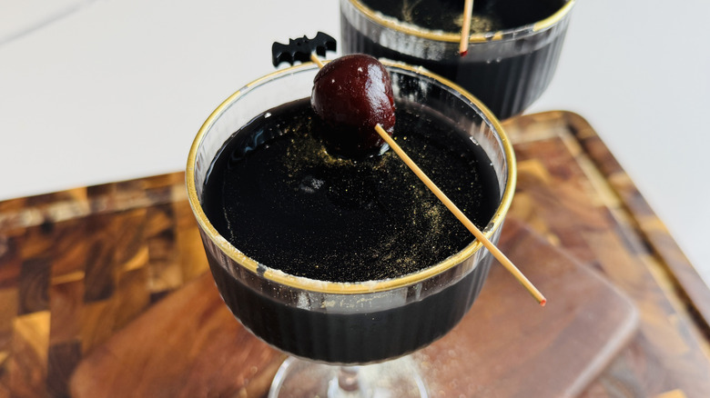 Black magic Halloween cocktail garnished with cherry and gold luster dust
