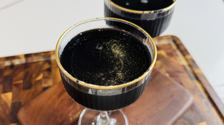 Black cocktail with gold luster dust in glass