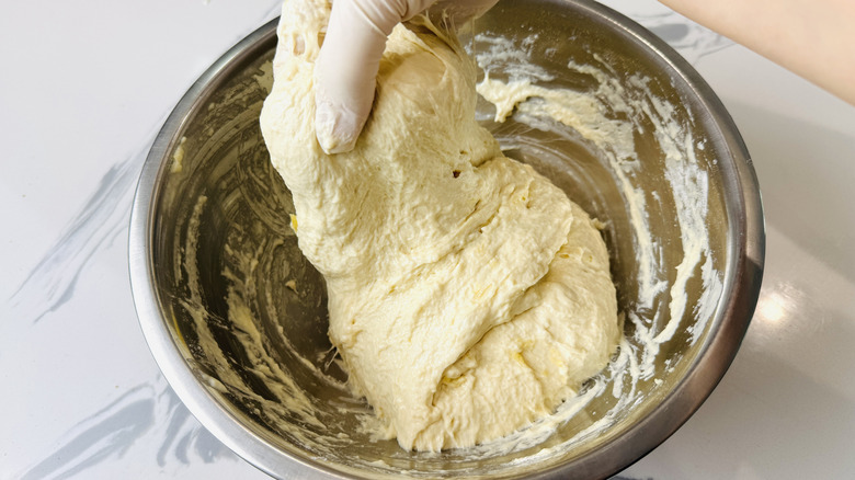 Gloved hand stretching dough in bowl