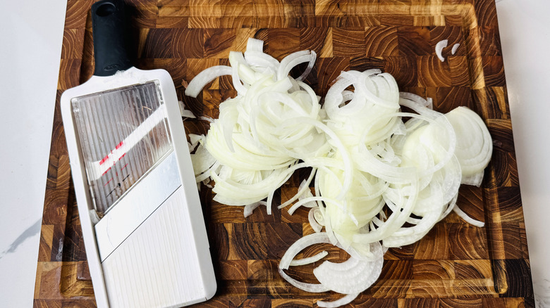 Mandoline and thinly sliced onion on wooden board
