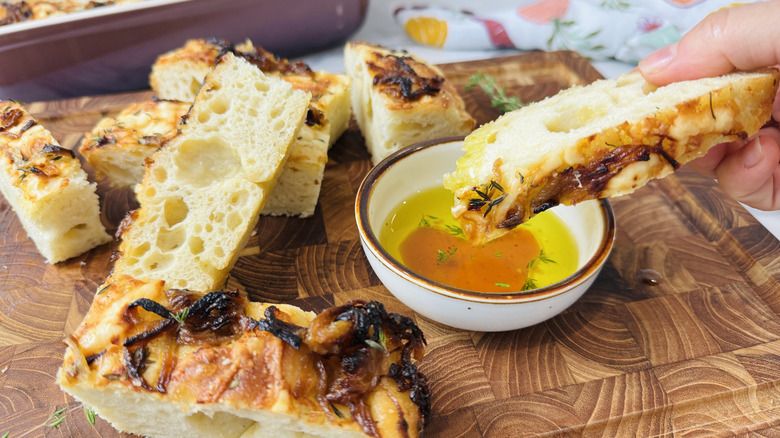 Hand dunking focaccia piece into olive oil next to more pieces of bread