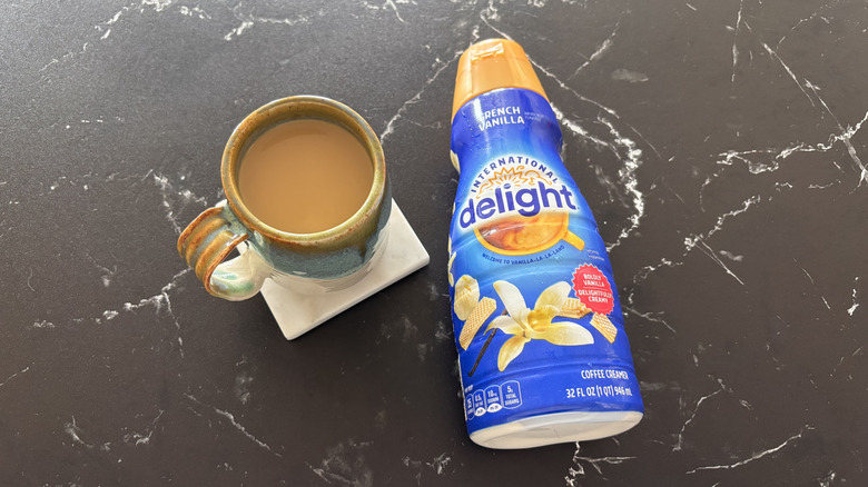 International Delight French Vanilla Creamer lying down next to a cup of coffee.