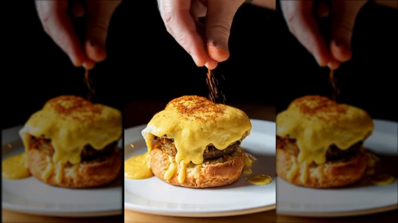 Hand sprinkling paprika on top of a crab eggs Benedict