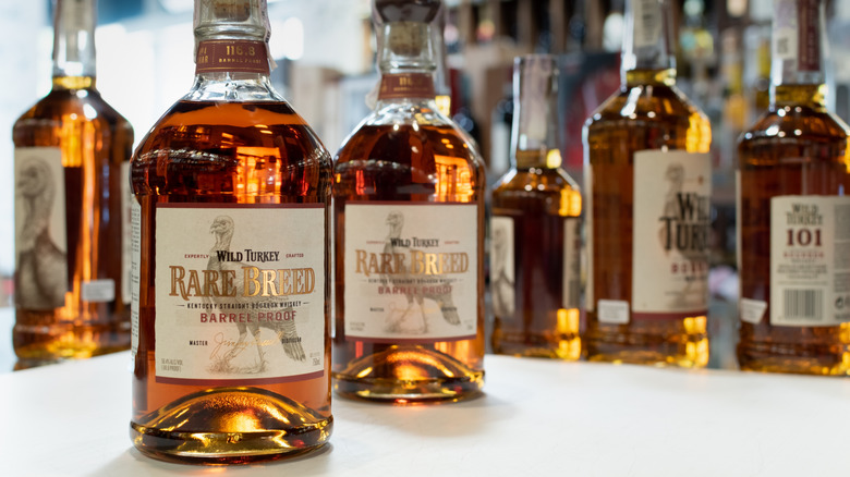 Two bottles of Wild Turkey Rare Breed placed on a table with more bottles shown in a blurred background