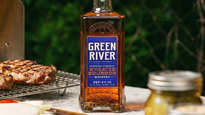 A bottle of Green River Wheated Bourbon placed outside surrounded by a barbecue setting