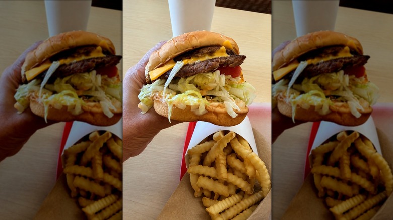 Hand holding Double Del Cheeseburger with fries and drink in background