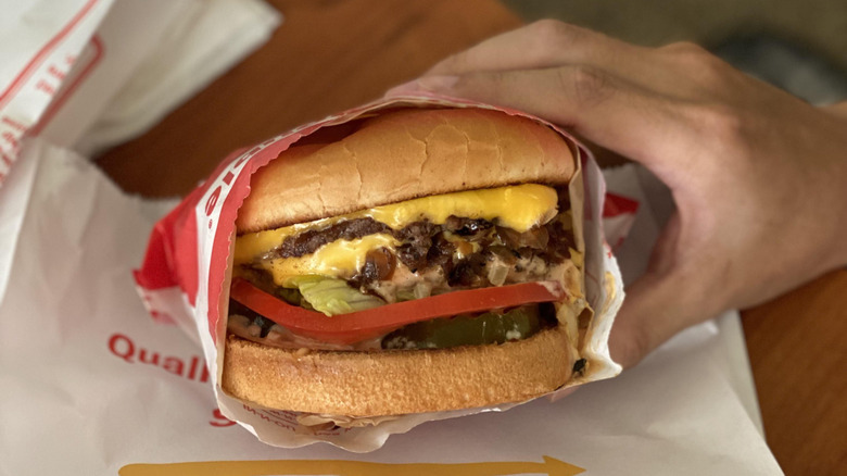Hand holding a half-wrapped In-N-Out Double Double above the paper bag it came in