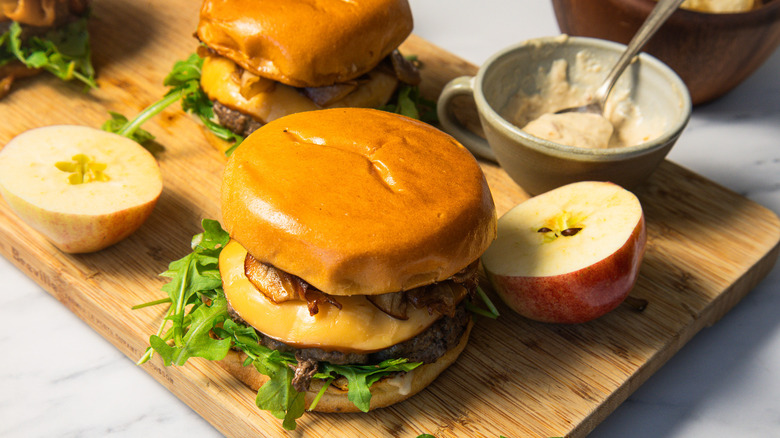 Two caramelized apple burgers on a cutting board with apples