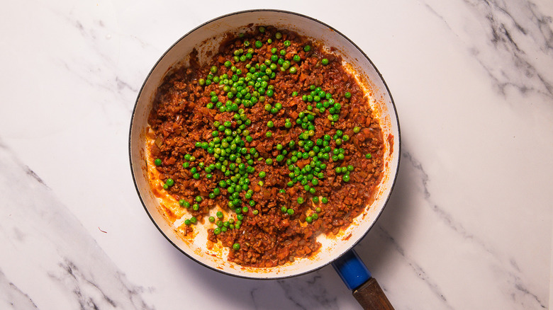 Meat ragu with peas in tomato sauce in pan