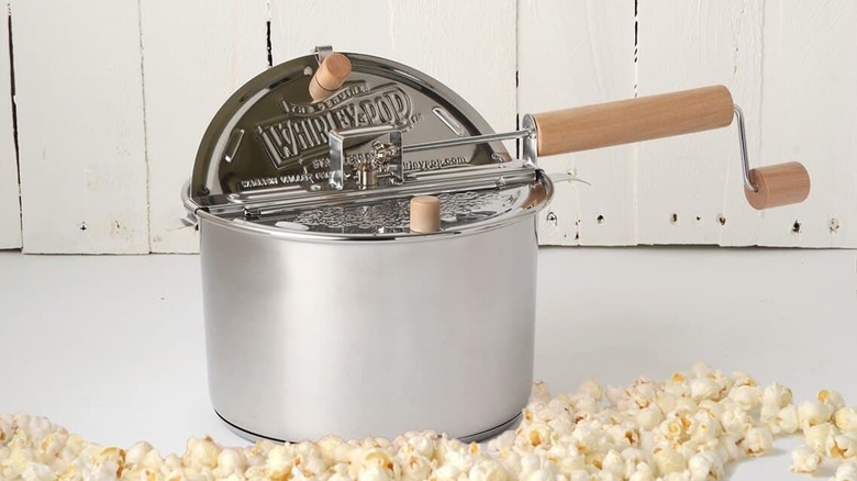 A stainless steel Whirley Pop stovetop popcorn maker next to a pile of popcorn