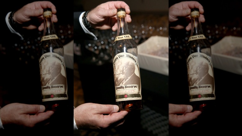 Hand holding a bottle of Pappy Van Winkle 23-year in front of glasses blurred in the background