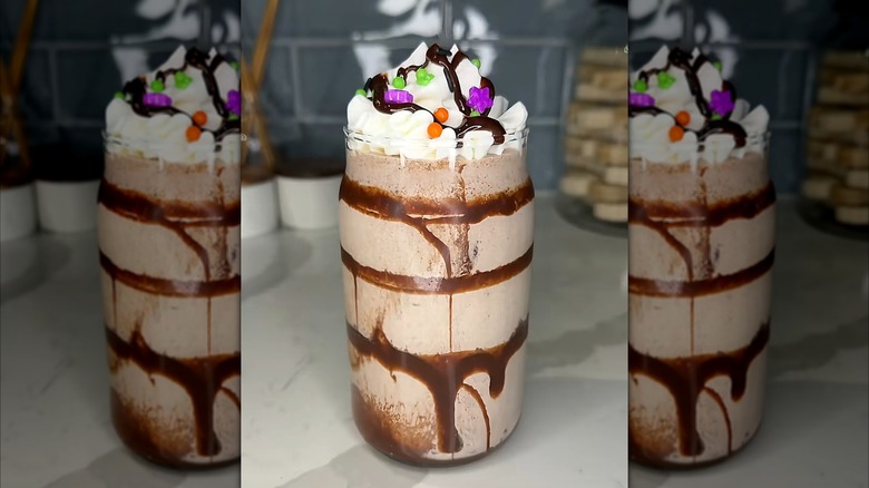 Chocolate milkshake with chocolate syrup in tall glass topped with whipped cream and Halloween-themed sprinkles