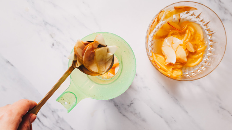 Ladling fruit into a pitcher besides bowl of sangria