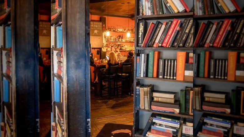 Bookcase opened to reveal secret bar inside, where bartender is shaking a cocktail for customers