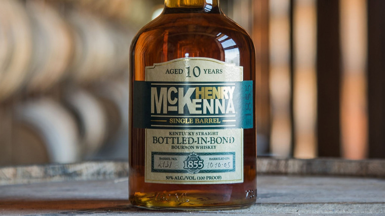 A bottle of Henry McKenna Single Barrel Bottled-in-Bond posed on top of a barrel in a warehouse