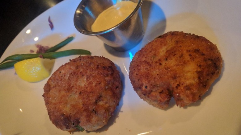 Two crab cakes on plate with sauce and lemon