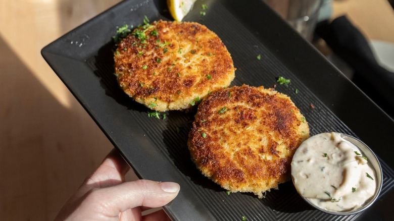 Two crab cakes on black plate with tartar