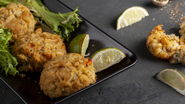 Crab cakes on black plate with lime and greens
