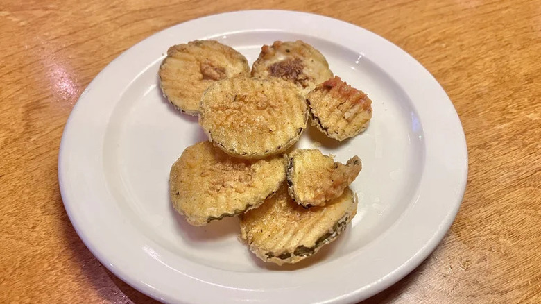 Some golden fried, crinkle cut pickle chips on a white plate