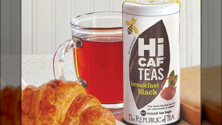 A cup of tea and a croissant near a container of HiCaf tea.