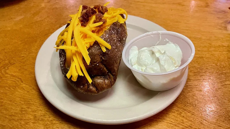 A loaded baked potato from Texas Roadhouse, sitting on a white plate on a polished wooden table
